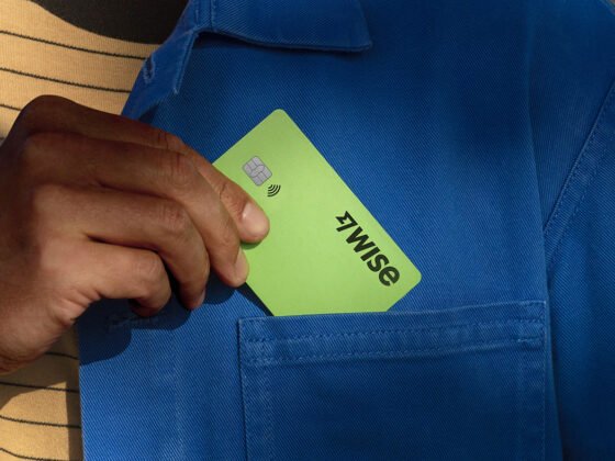 Homem com camiseta amarela e camisa azul colocando o cartão verde da Wise no bolso da camisa
