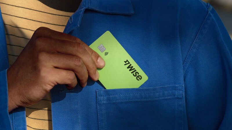 Homem com camiseta amarela e camisa azul colocando o cartão verde da Wise no bolso da camisa